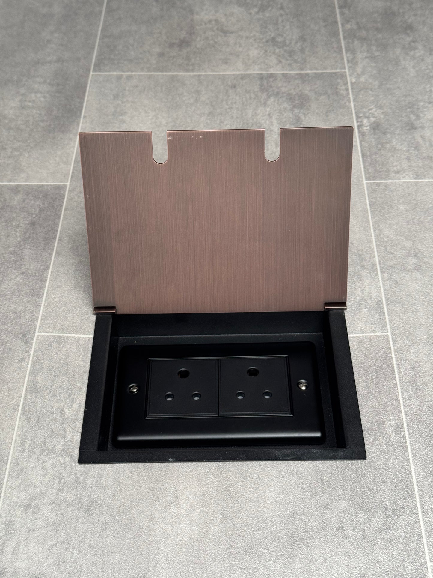 Recessed floor socket with antique copper finish, opened to show the double 5 amp round pin socket inside.