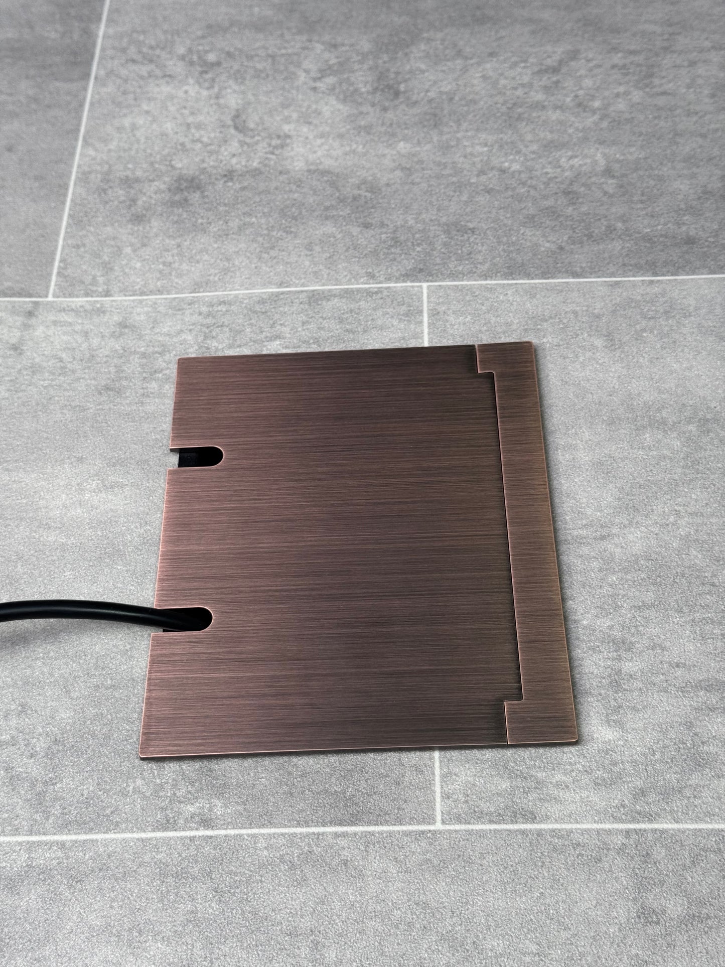 Double Antique Copper Recessed Floor Socket With Lid Closed Flat Showing Just Cable Coming Out If The Socket - Side On View.