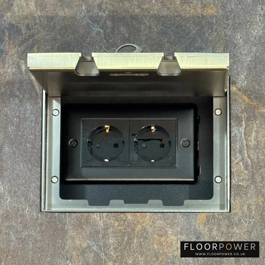 Antique Brass Double Recessed Flush Floor Socket with Schuko Plug Socket n a stone floor.