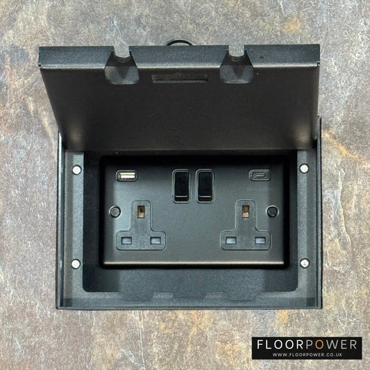Matt Black Double Recessed Flush Floor Socket with USB A + C Plug Socket n a stone floor.