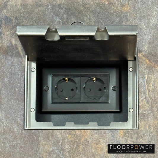 Old Bronze Double Recessed Flush Floor Socket with Schuko Plug Socket n a stone floor.