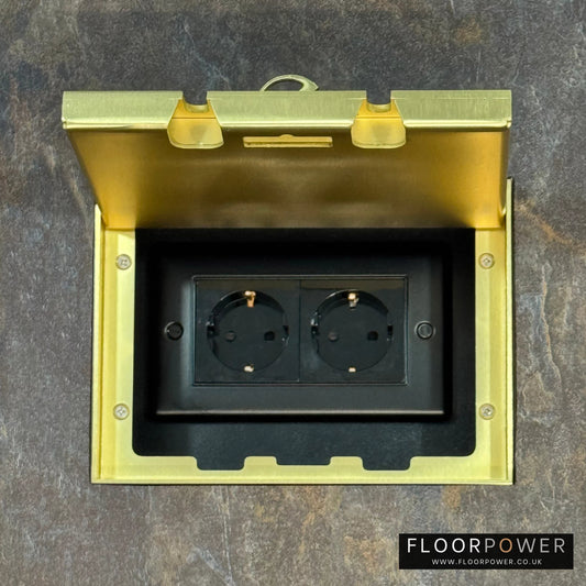 Satin Brass Double Recessed Flush Floor Socket with Schuko Plug Socket n a stone floor.