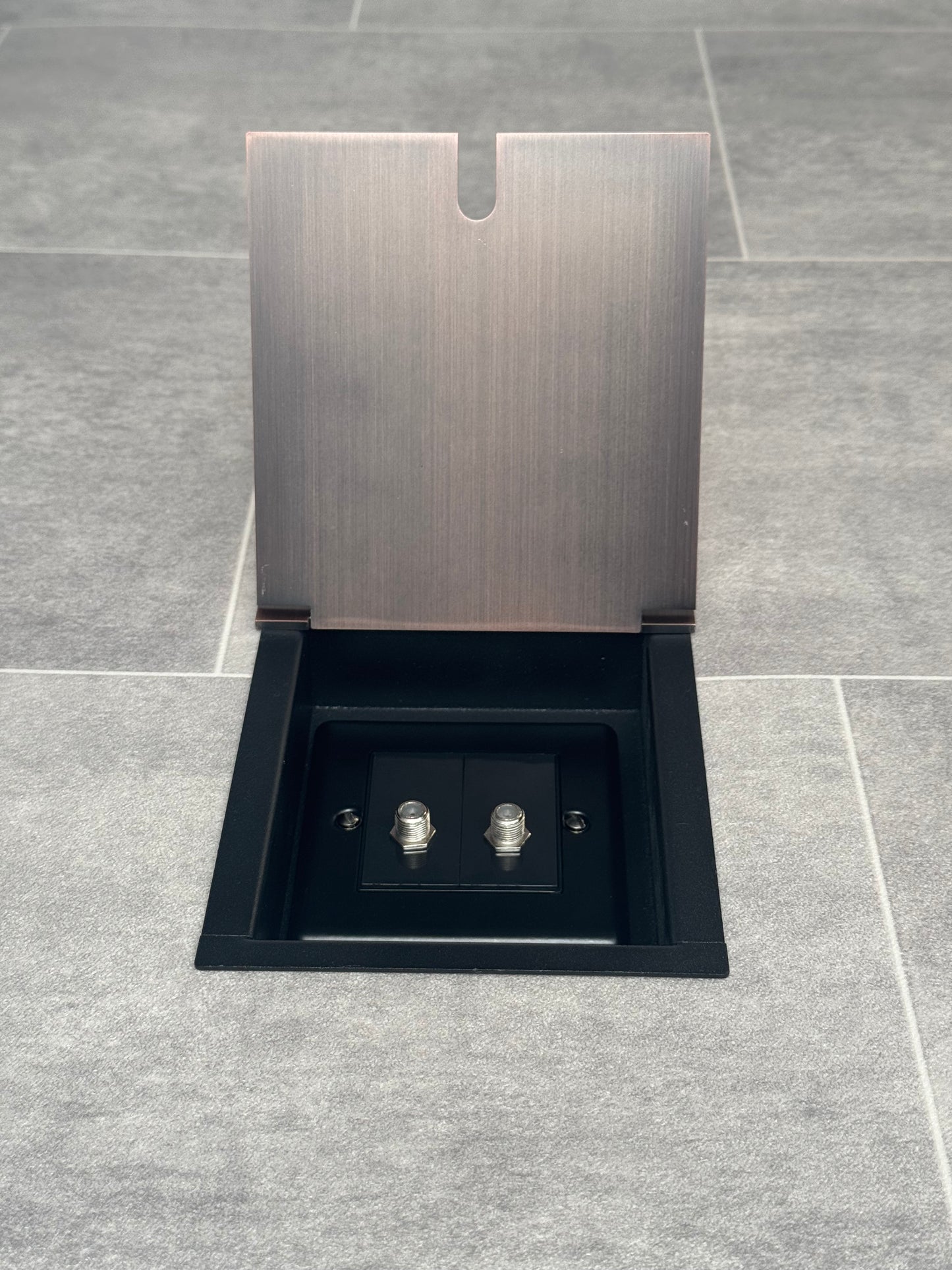 Recessed floor socket with antique copper finish, consisting of a single gang box and a 2 gang satellite socket, installed in a tiled floor.