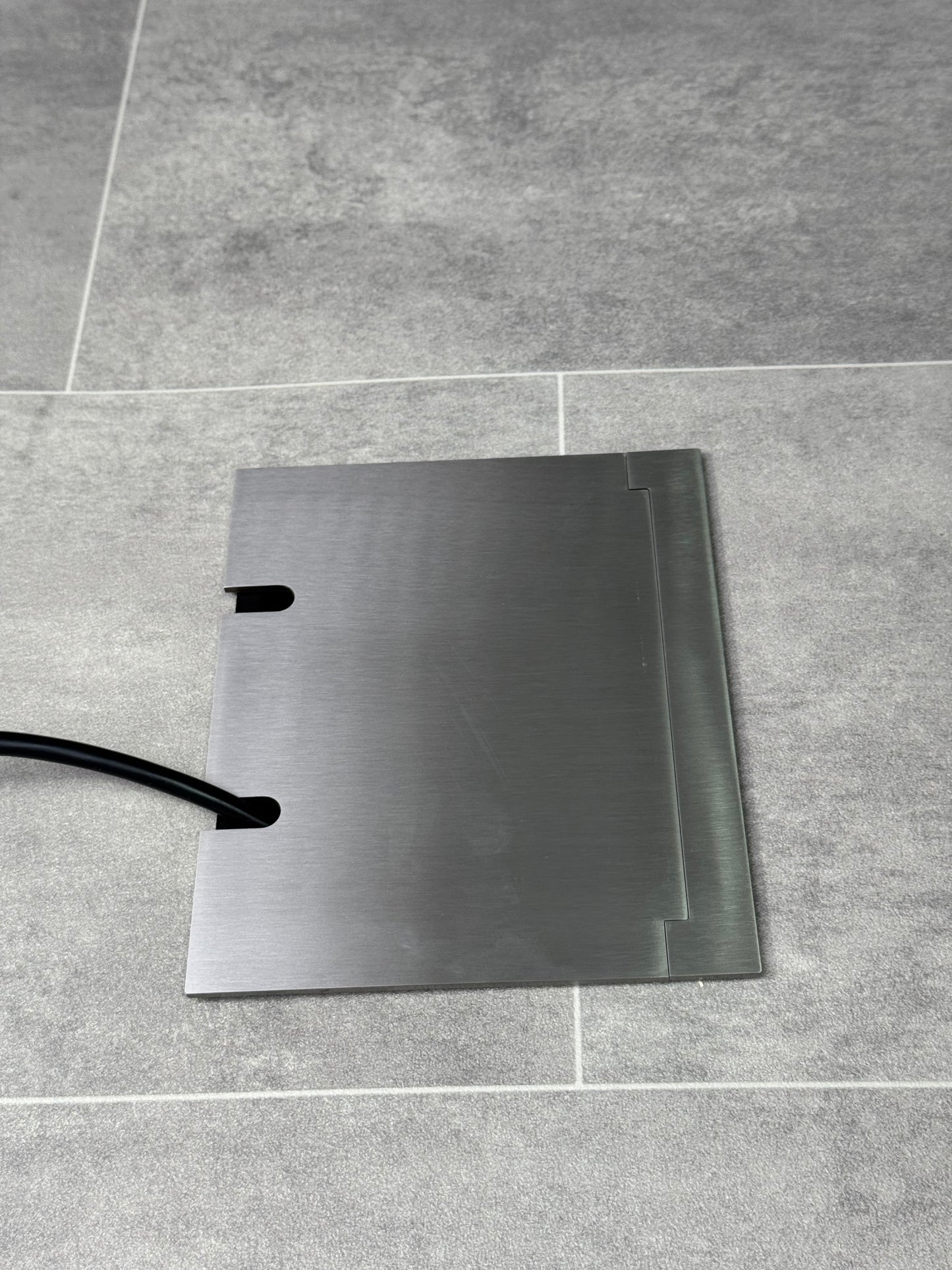 Double Satin Stainless Recessed Floor Socket With Lid Closed Flat Showing Just Cable Coming Out If The Socket - Side On View.