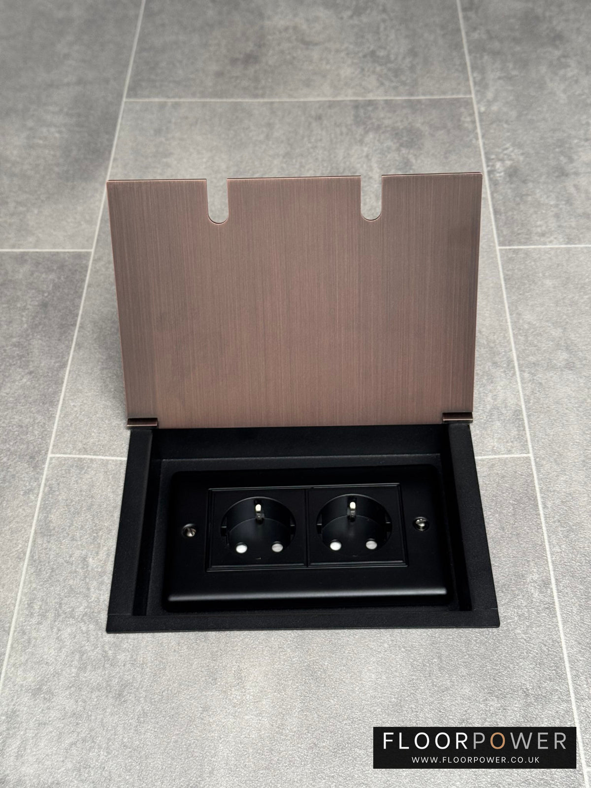 Antique copper double recessed floor socket with two Schuko (European) sockets in a black base installed in a floor.