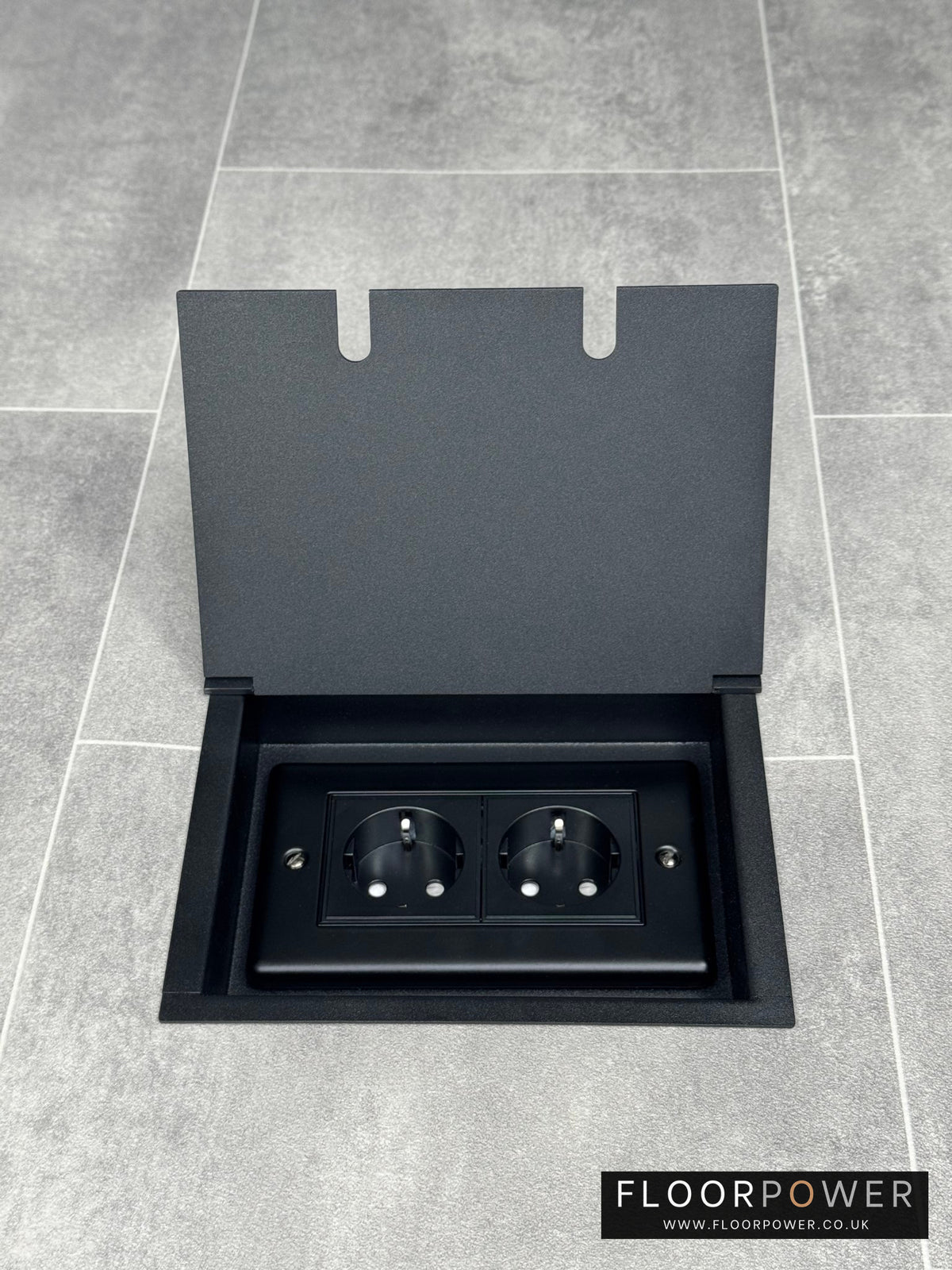 A matt black recessed floor socket opened to reveal a double 13 amp unswitched Schuko socket.