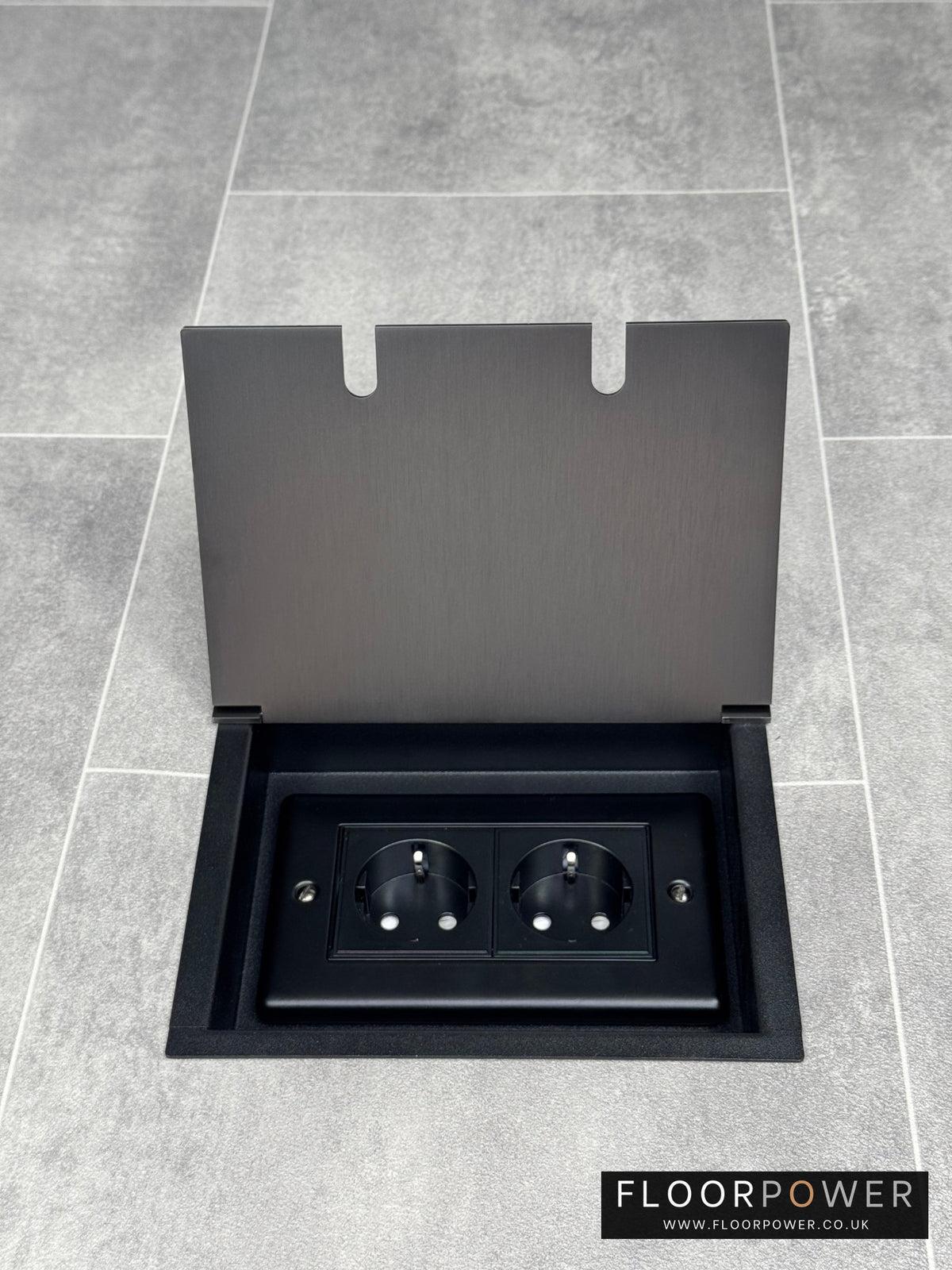 Old bronze double recessed floor featuring a double gang design with two Schuko outlets, set into a grey tiled floor.