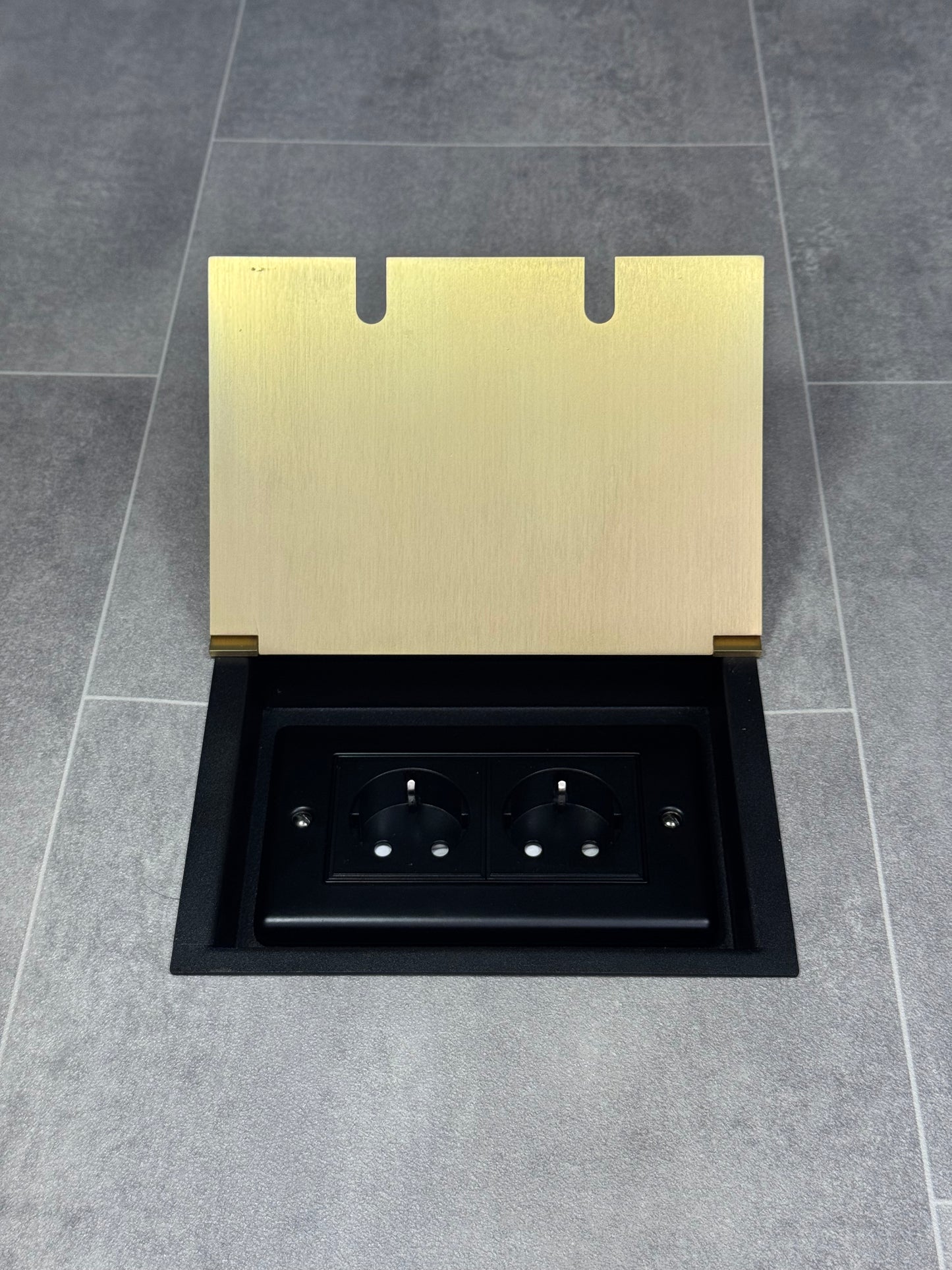 A satin brass double recessed floor socket with two Schuko (European) sockets in a black base installed in a floor.