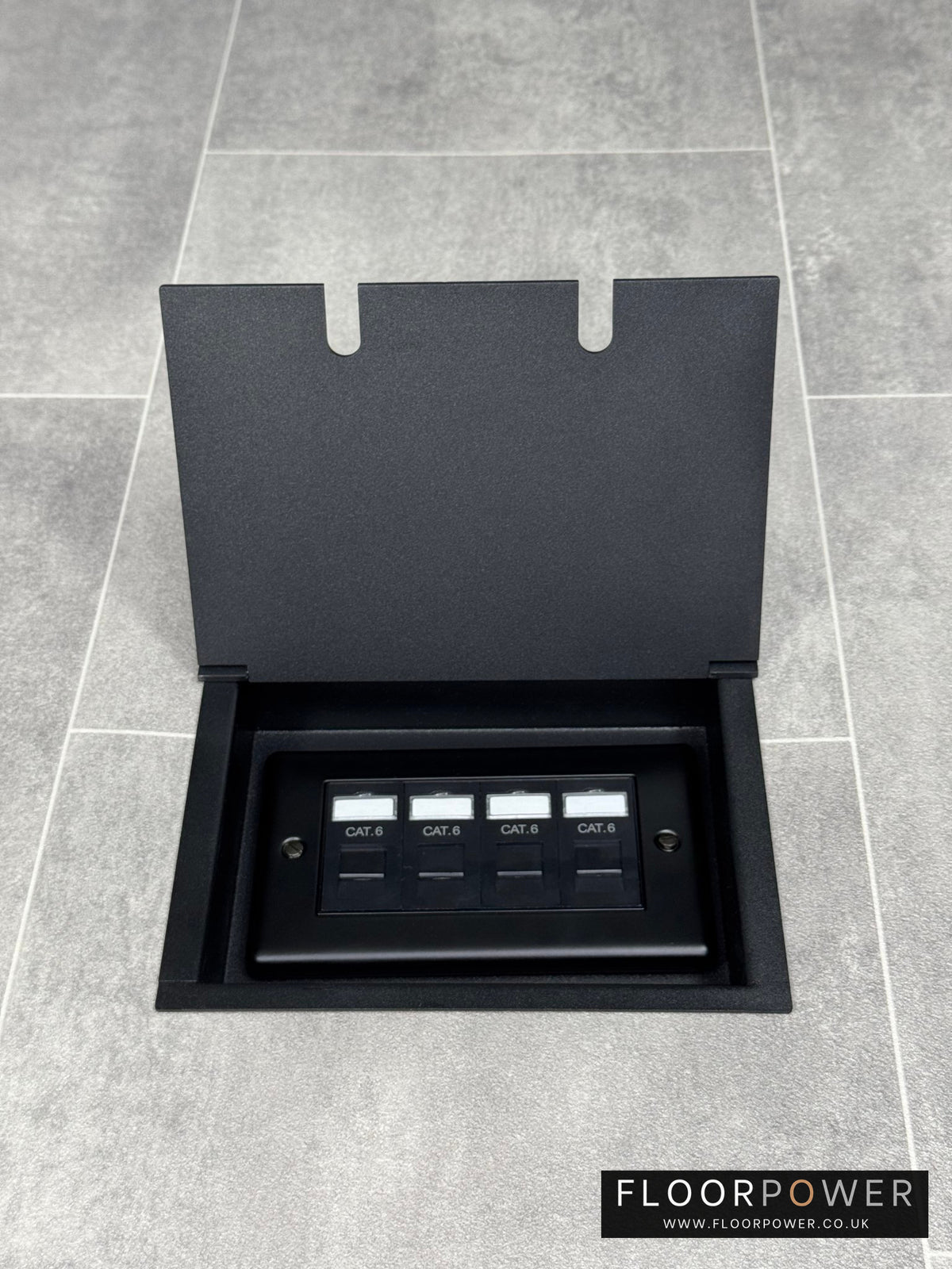 A matt black double recessed floor socket with a black base installed on a grey floor, opened to show the 4 gang RJ45 cat6 socket.