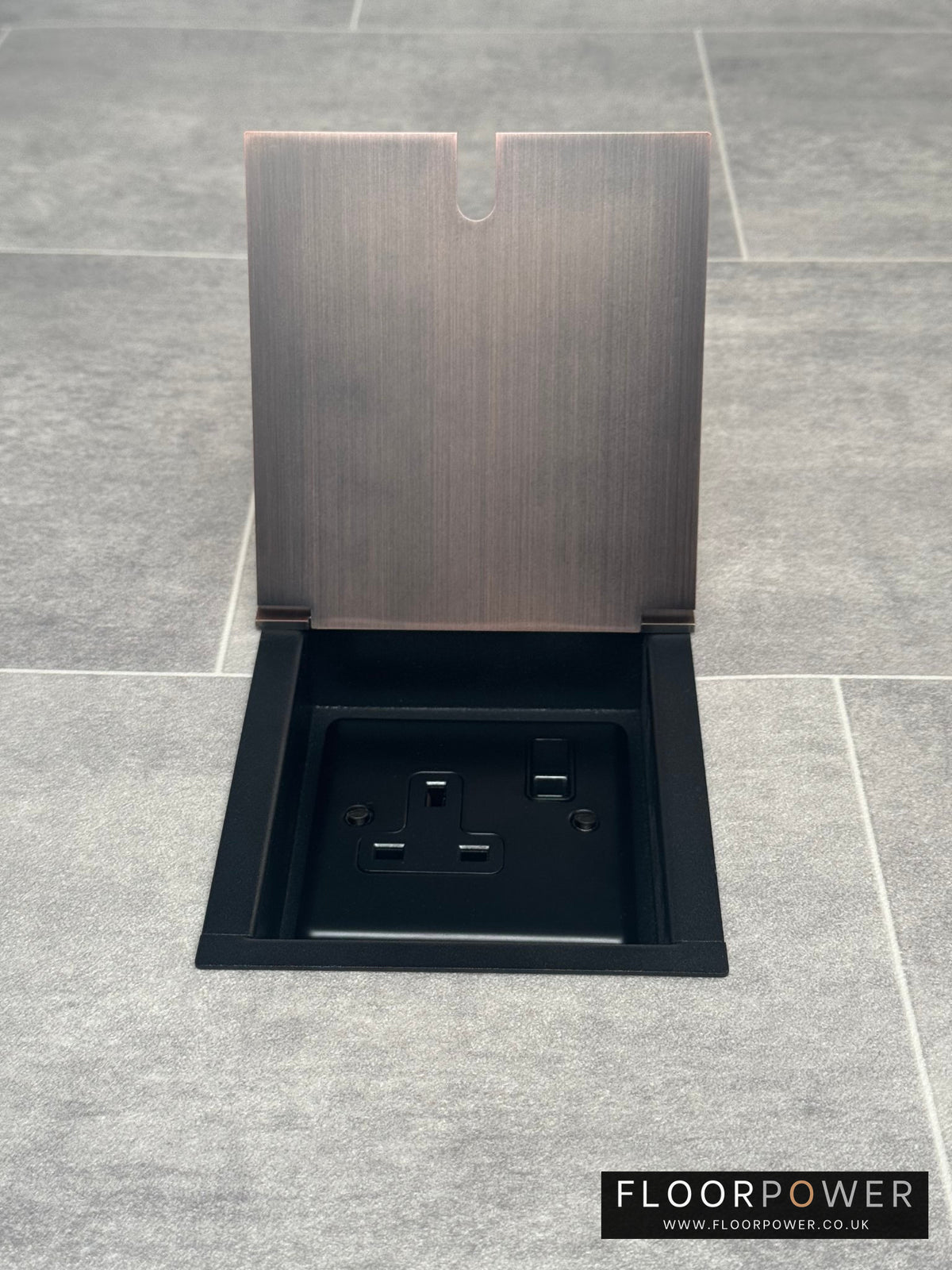A recessed floor socket with a antique copper finish, opened to show the 13 Amp plug socket.