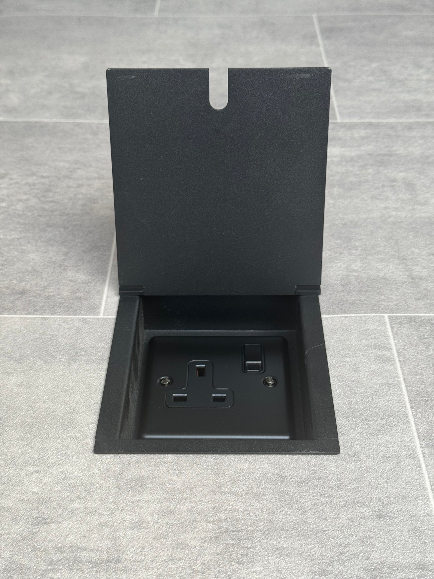 A matt black recessed floor socket with a single 13 amp switched plug point.