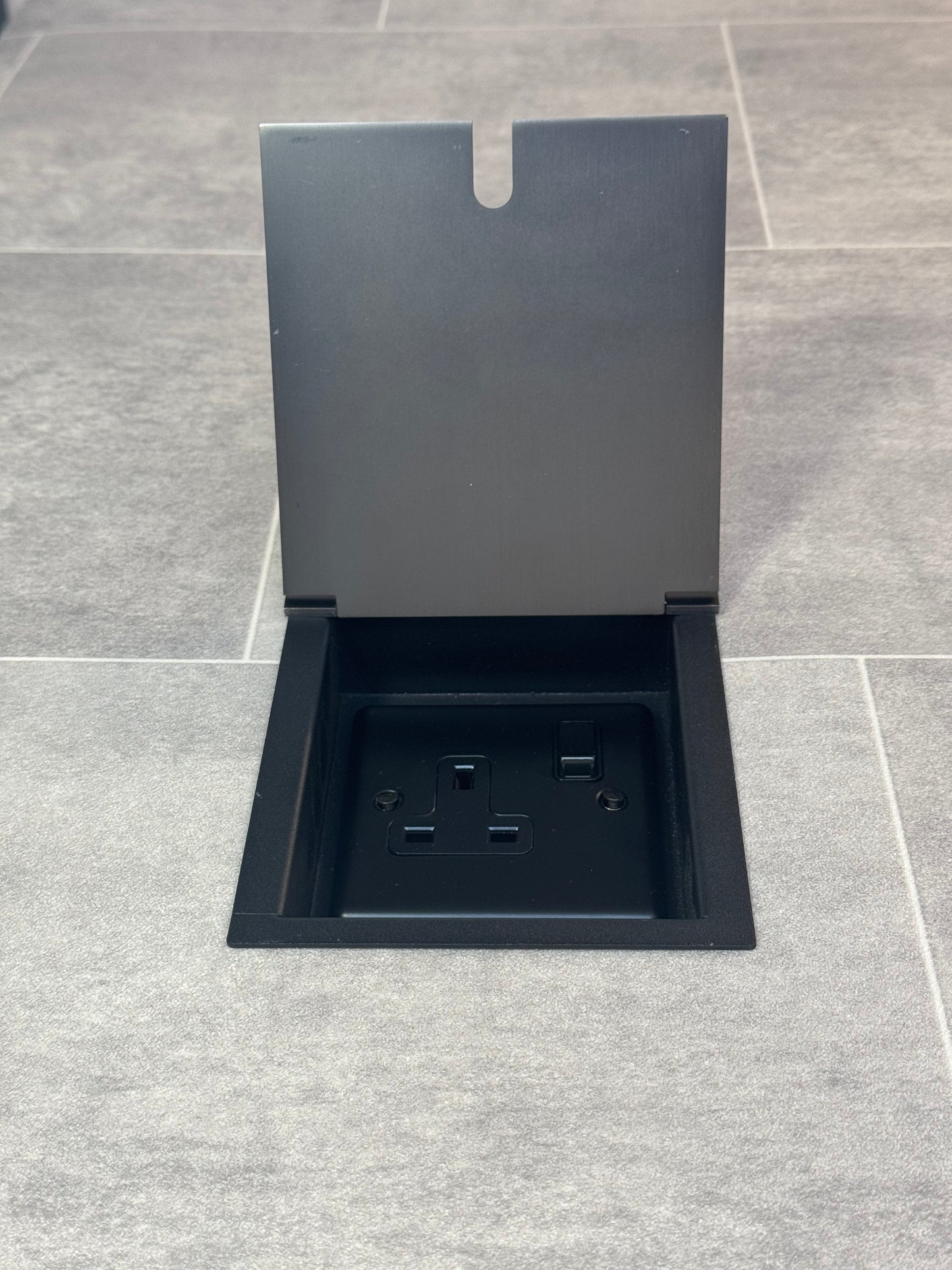 Old bronze single recessed floor socket with one 13 amp switched sockets in a black base, installed in a floor.