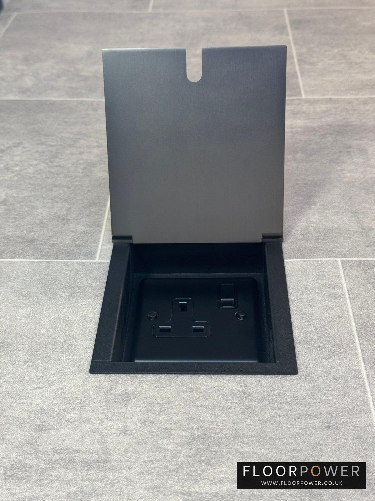 Old bronze single recessed floor socket with one 13 amp switched sockets in a black base, installed in a floor.