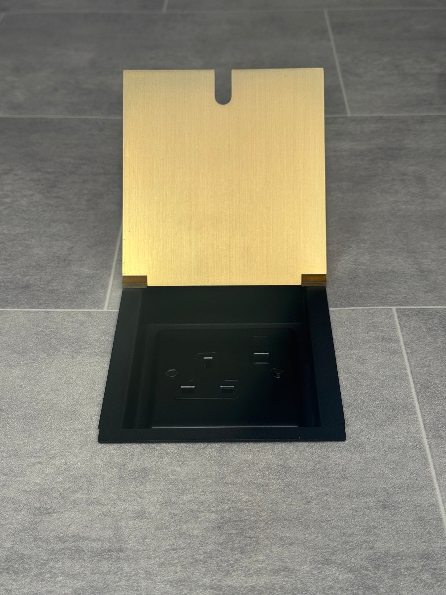 A satin brass single recessed floor socket with one 13 amp switched socket in a black base, installed in a floor.