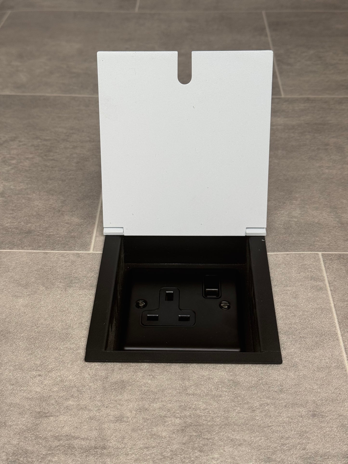 A white single recessed floor socket with one 13 amp switched socket in a black base, installed in a floor.