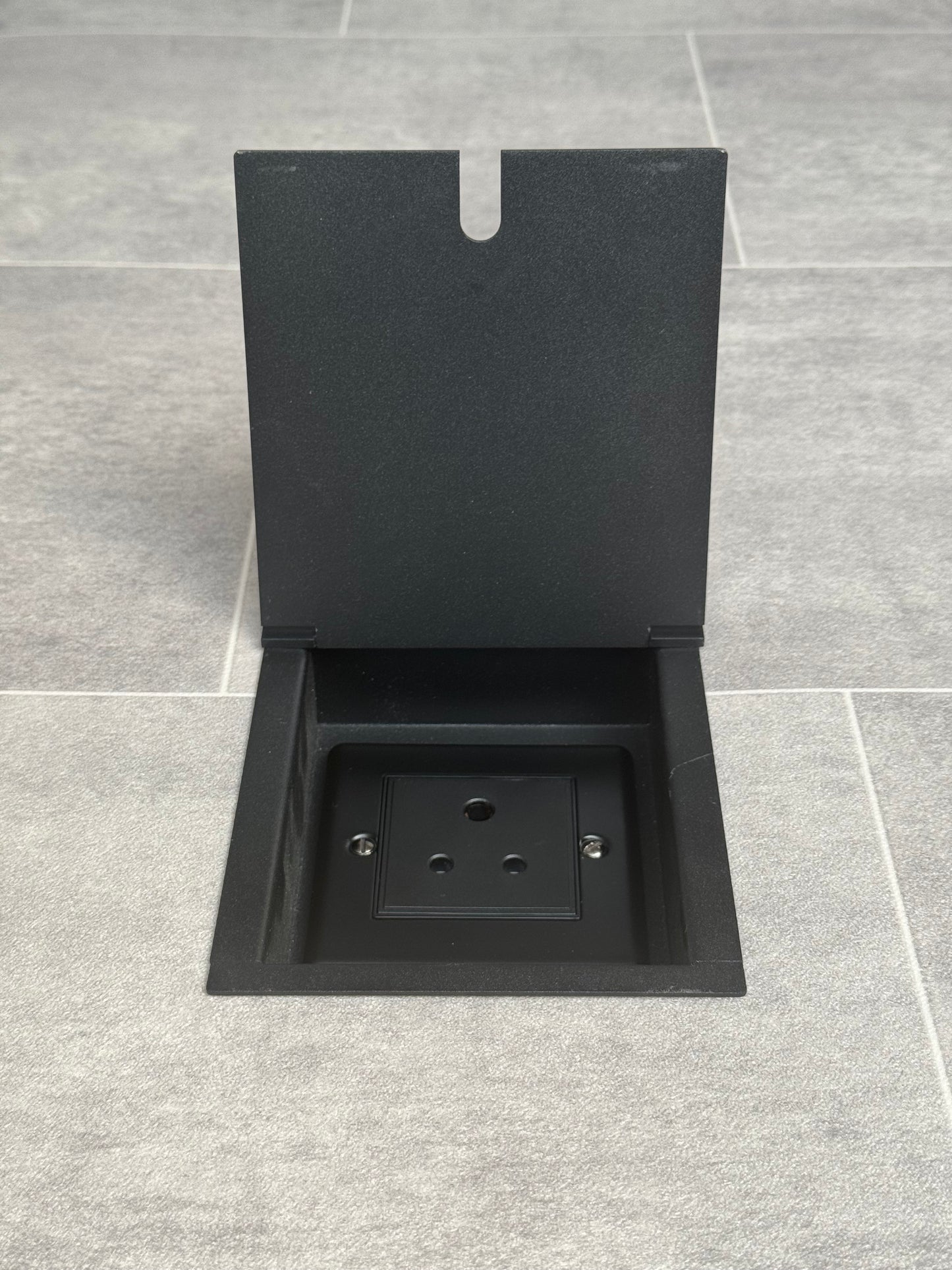 A matt black recessed floor socket with a single 5 amp round pin socket for lighting, installed in a tiled floor.