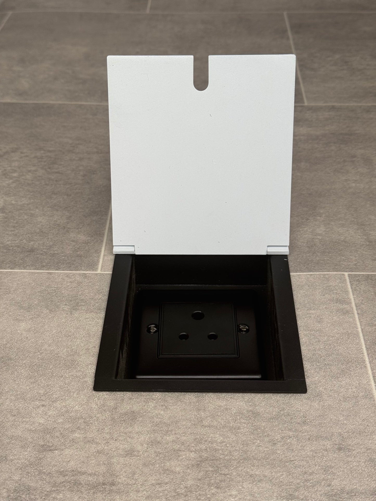 A white recessed floor socket with a single 5 amp round pin socket for lighting, installed in a tiled floor.