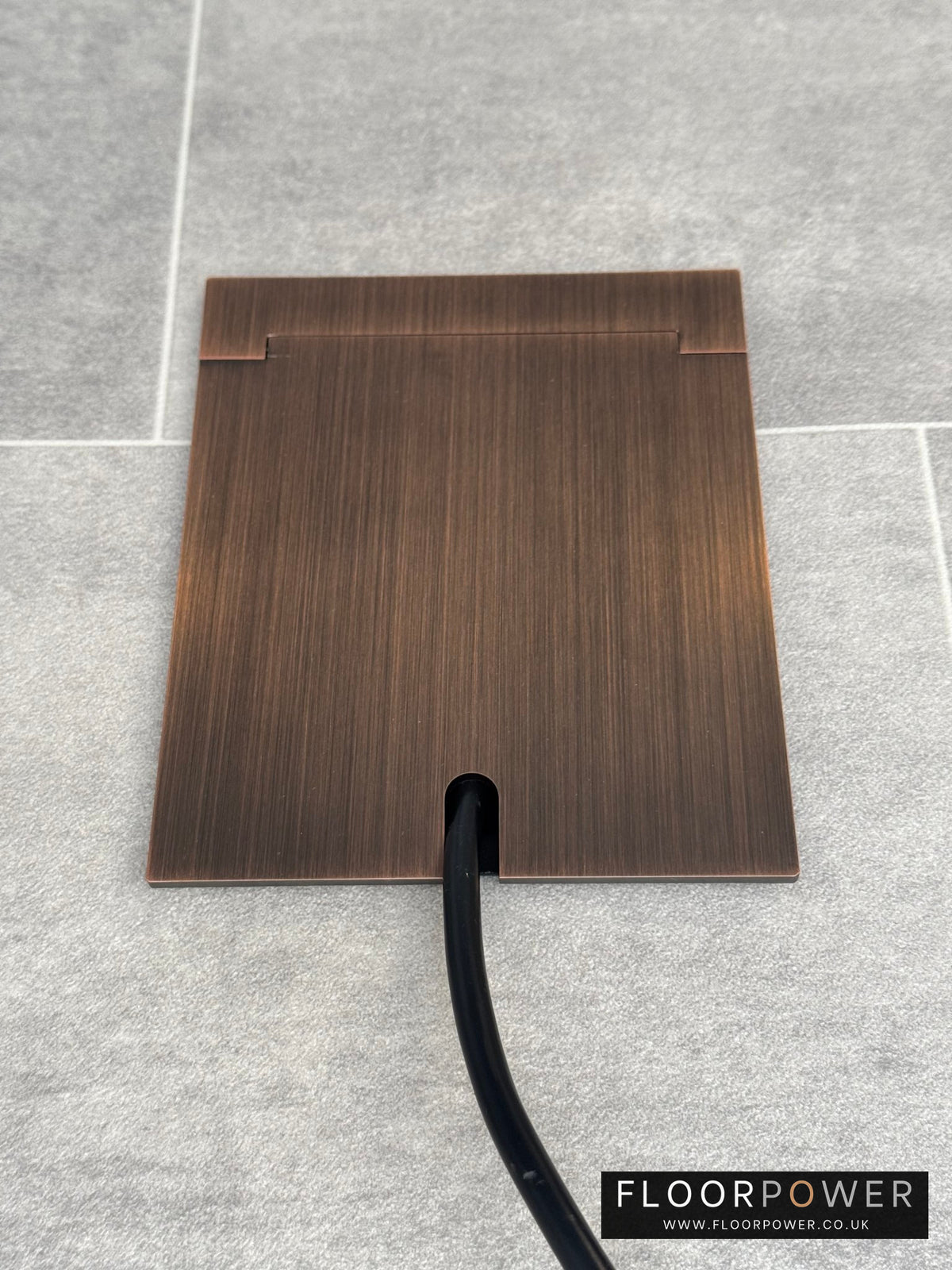 Single Antique Copper Recessed Floor Socket With Lid Closed Flat Showing Just Cable Coming Out If The Socket - Front On View.
