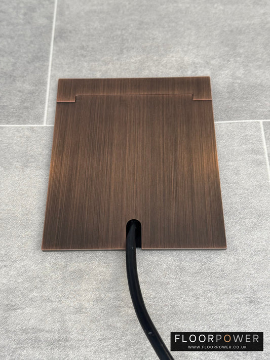 Single Antique Copper Recessed Floor Socket With Lid Closed Flat Showing Just Cable Coming Out If The Socket - Front On View.