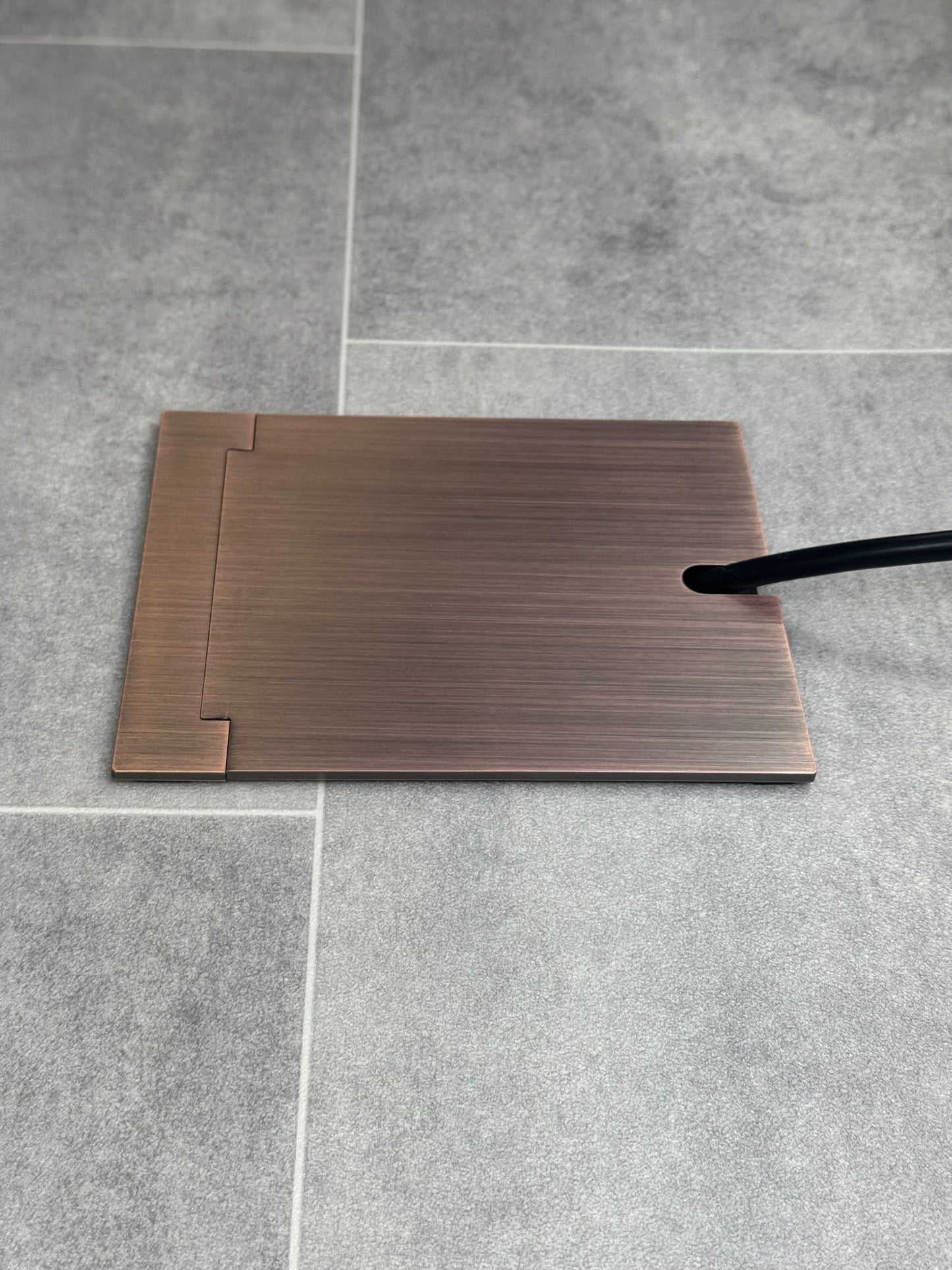Single Antique Copper Recessed Floor Socket With Lid Closed Flat Showing Just Cable Coming Out If The Socket - Side On View.