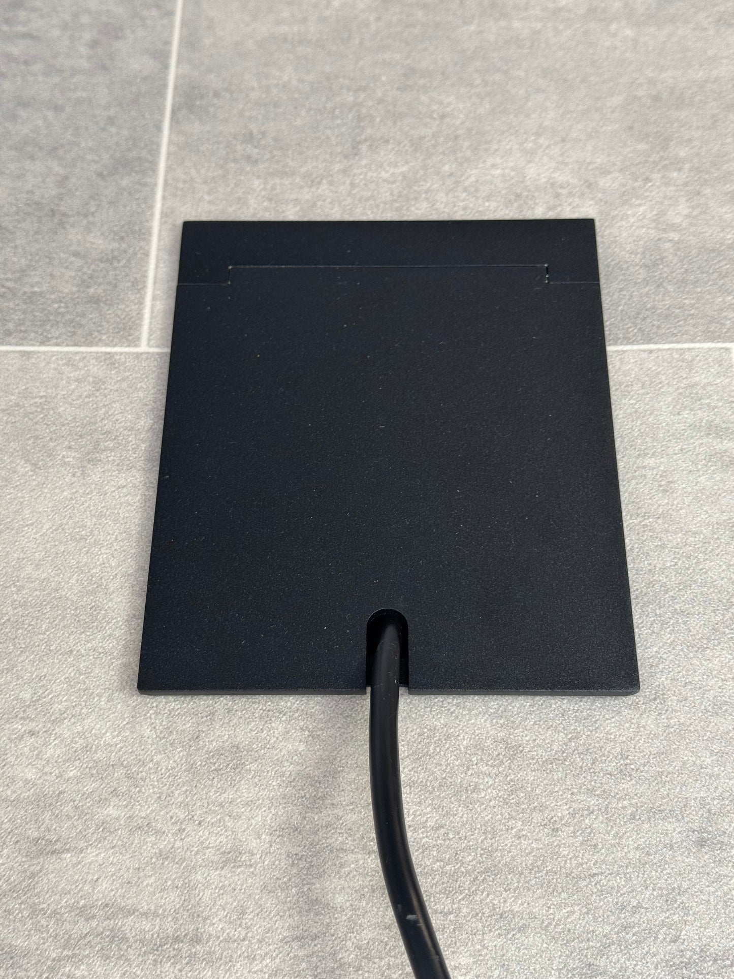 Single Matt Black Recessed Floor Socket With Lid Closed Flat Showing Just Cable Coming Out If The Socket - Front On View.
