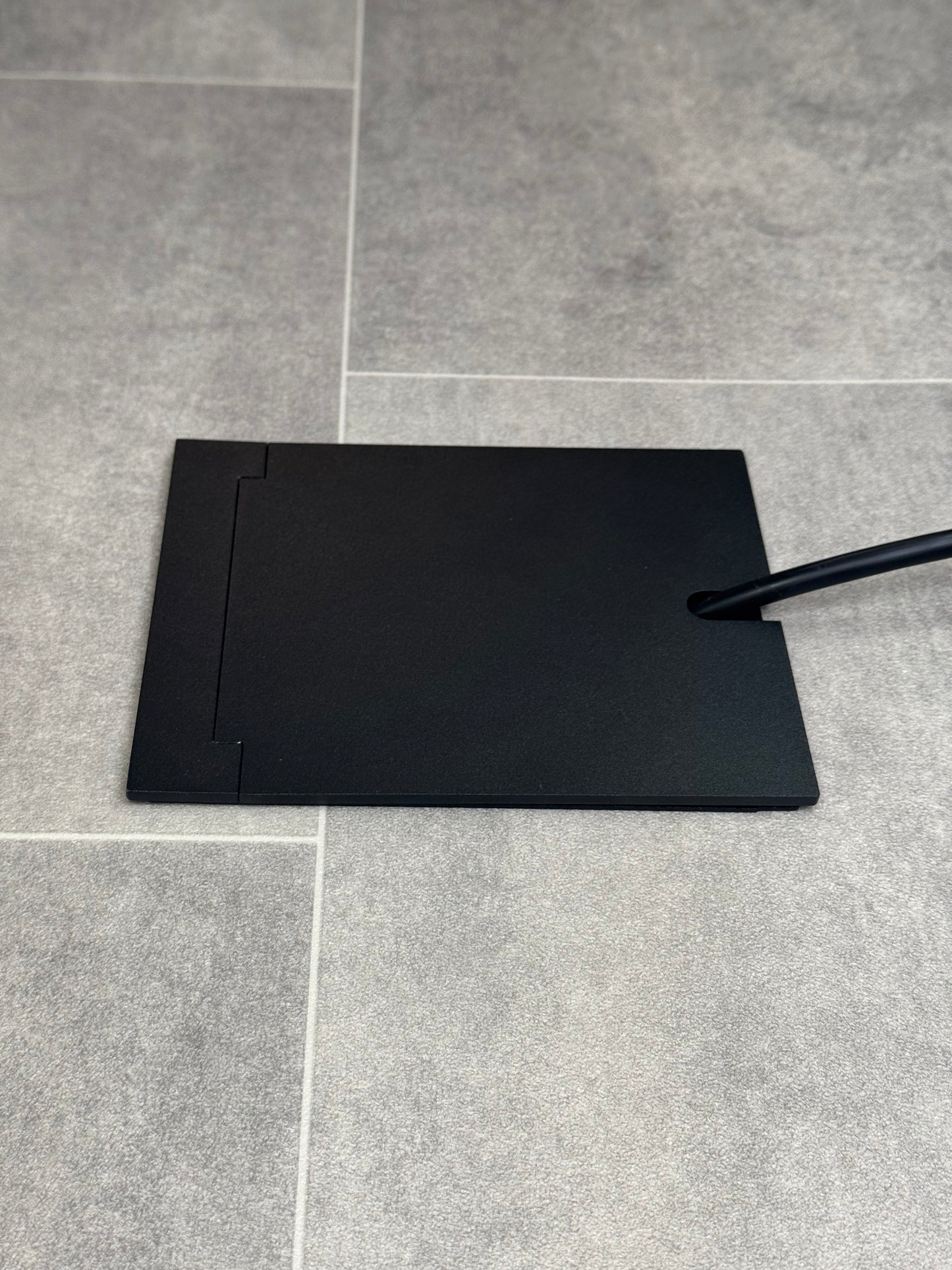 Single Matt Black Recessed Floor Socket With Lid Closed Flat Showing Just Cable Coming Out If The Socket - Side On View.