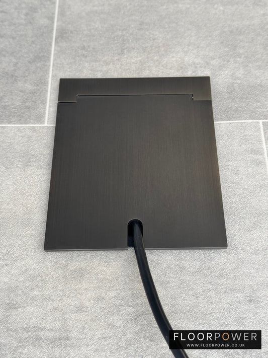 Single Old Bronze Recessed Floor Socket With Lid Closed Flat Showing Just Cable Coming Out If The Socket - Front On View.