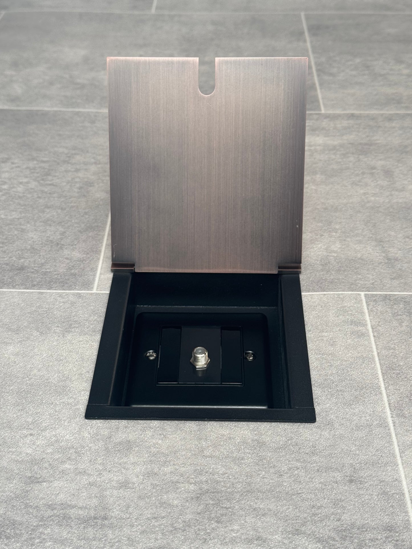 A antique copper recessed floor socket with a single satellite socket, installed on a grey floor.