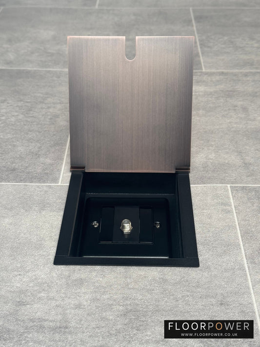 A antique copper recessed floor socket with a single satellite socket, installed on a grey floor.