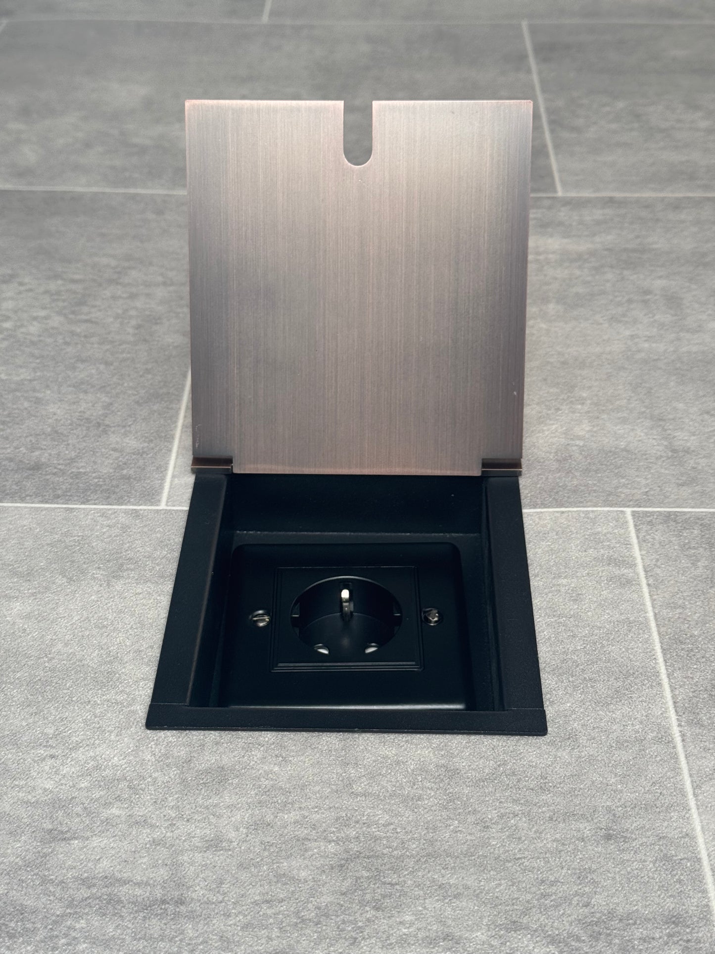 Recessed floor socket in antique copper color installed in a floor tile, with the cover opened to reveal the 13amp Schuko Socket.