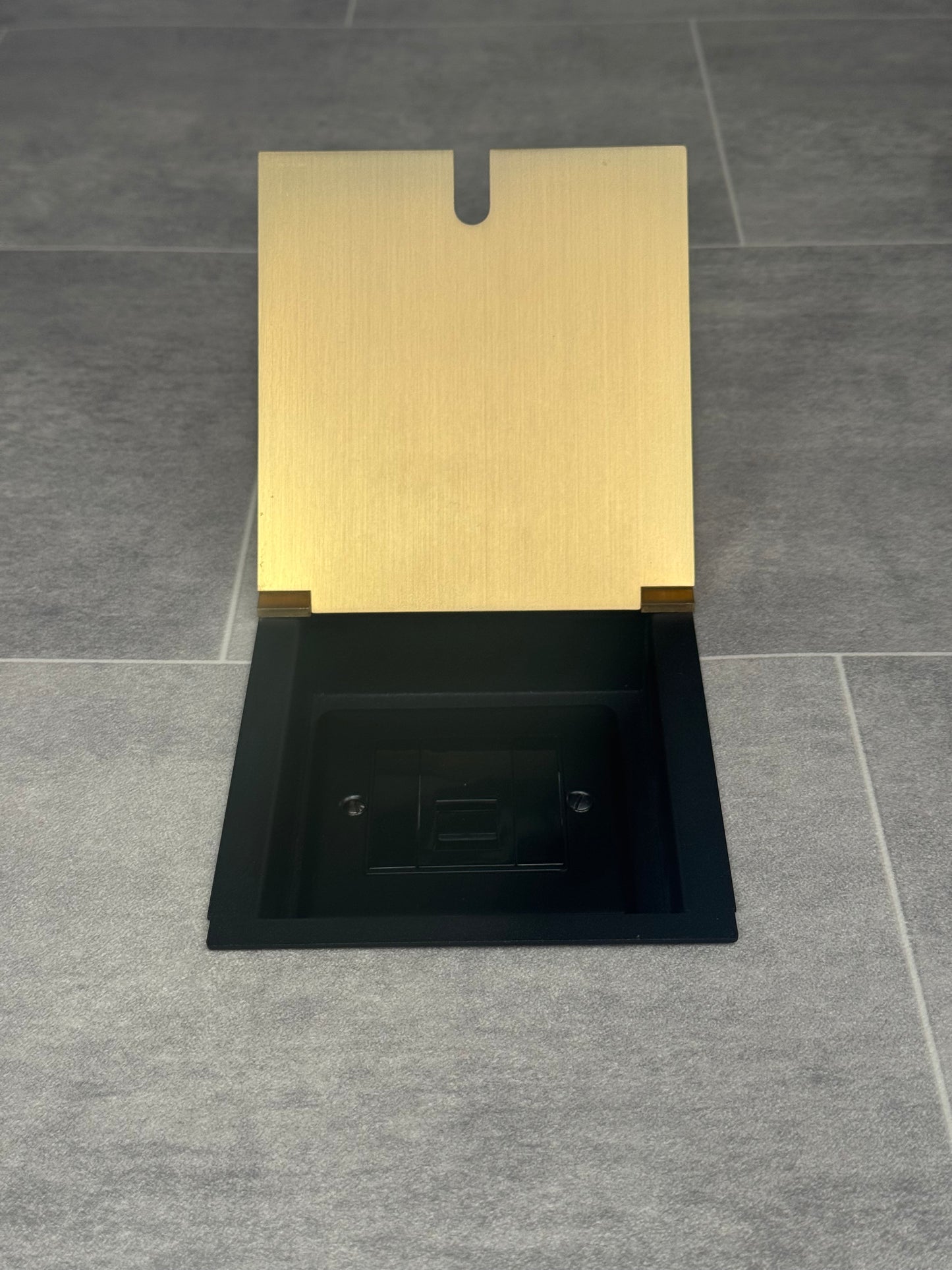 A satin brass recessed floor socket with a UK phone socket installed into a tiled floor.