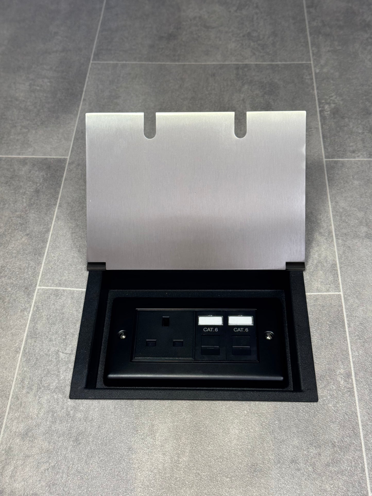 A satin stainless steel double recessed floor socket with a 13amp unswitched socket and 2 RJ45 sockets, set in a gray tiled floor.
