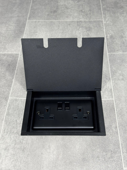 A matt black double recessed floor socket with a 13amp switched plug socket, in a tiled floor.