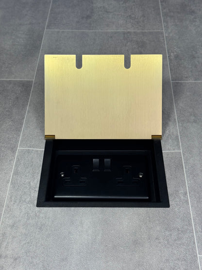 A satin brass double recessed floor socket with twin 13 amp switched sockets in a black base, installed in a floor.