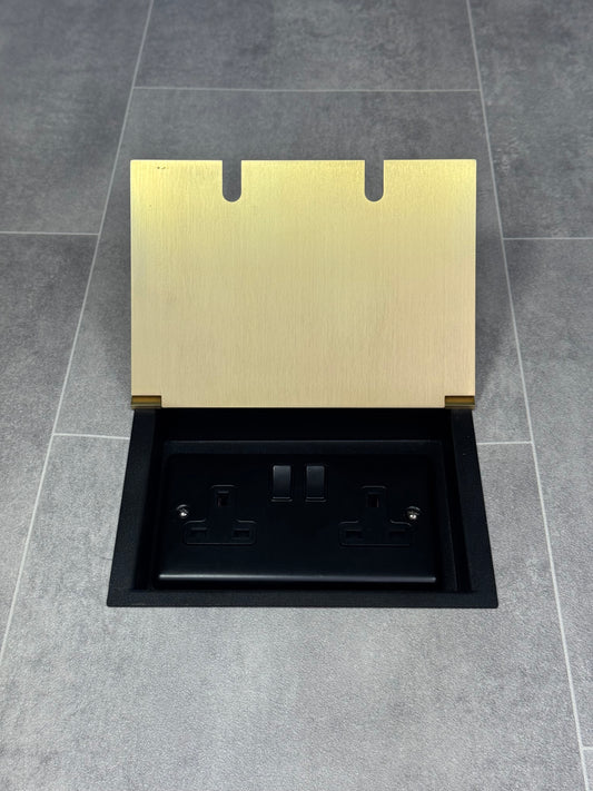 A satin brass double recessed floor socket with twin 13 amp switched sockets in a black base, installed in a floor.