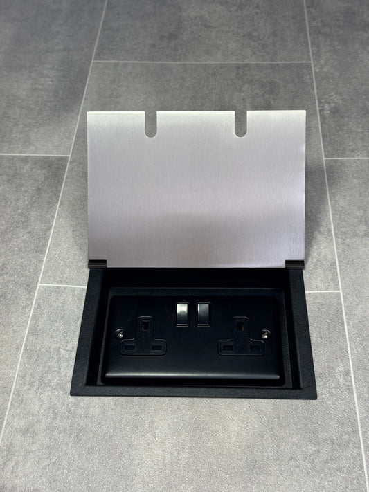 A satin stainless double recessed floor socket with twin 13 amp switched sockets in a black base, installed in a tiled floor.