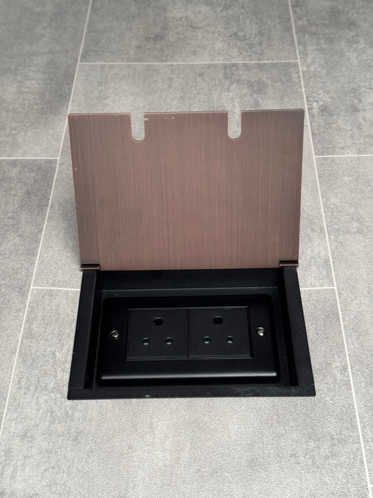 Recessed floor socket with antique copper finish, opened to show the double 5 amp round pin socket inside.