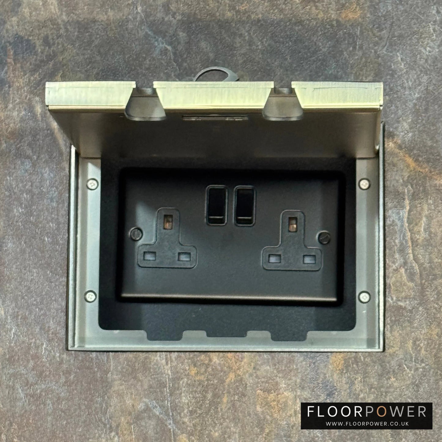 Antique Brass Double Recessed Flush Floor Socket with 13A Switched Plug Socket n a stone floor.