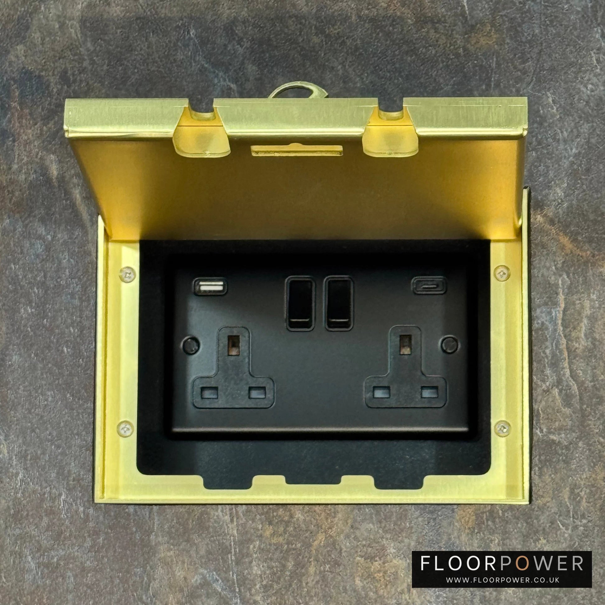 Satin Brass Double Recessed Flush Floor Socket with USB A + C Plug Socket n a stone floor.