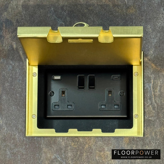 Satin Brass Double Recessed Flush Floor Socket with USB A + C Plug Socket n a stone floor.