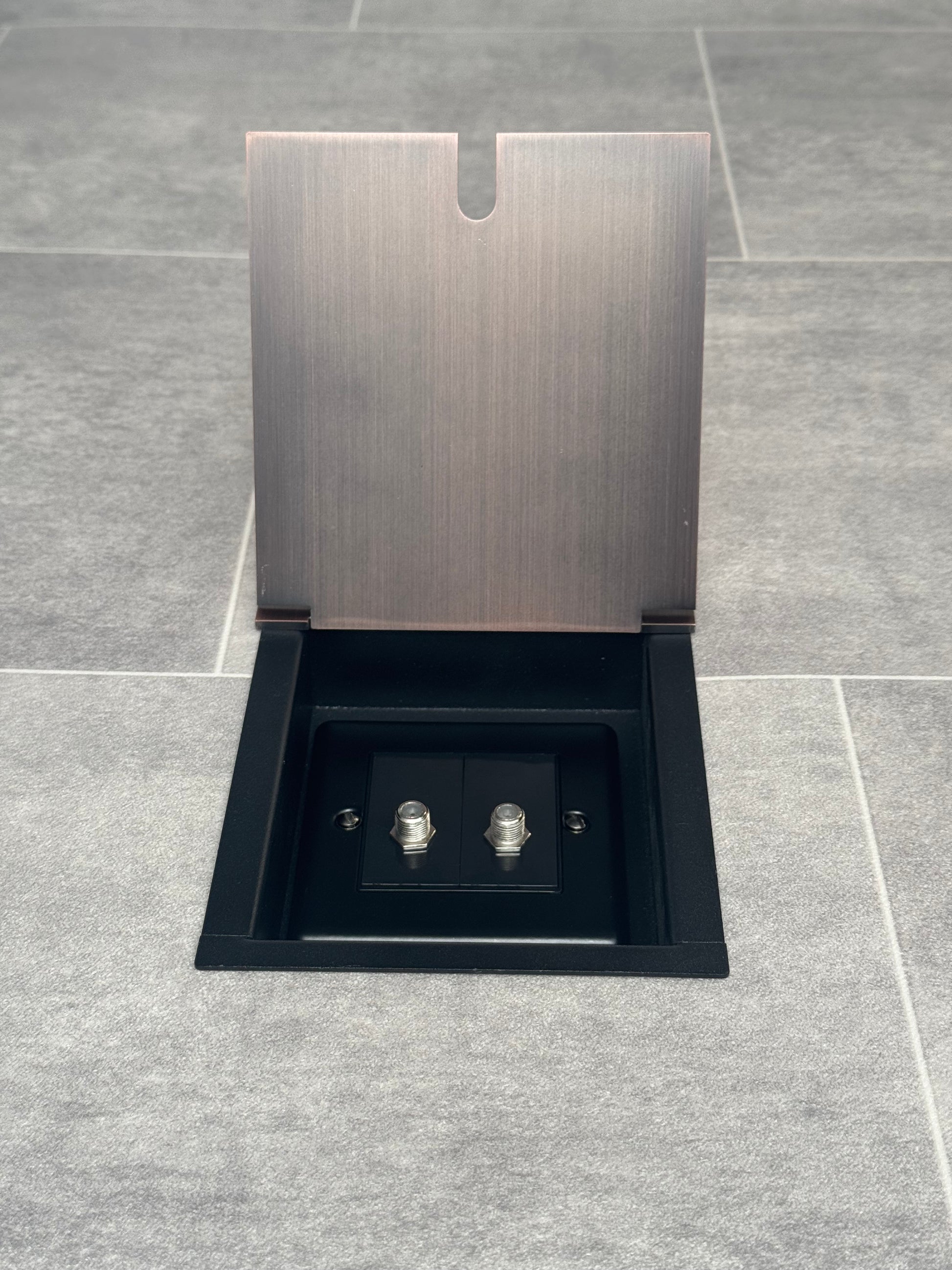 Recessed floor socket with antique copper finish, consisting of a single gang box and a 2 gang satellite socket, installed in a tiled floor.