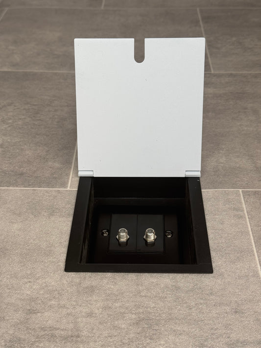 A white recessed floor socket with a 2 gang (double) satellite socket, set in a tiled floor.