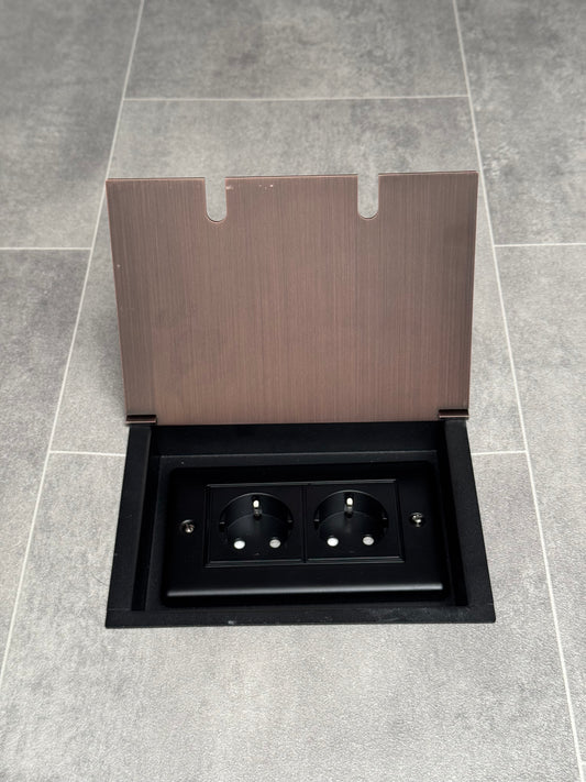 Antique copper double recessed floor socket with two Schuko (European) sockets in a black base installed in a floor.