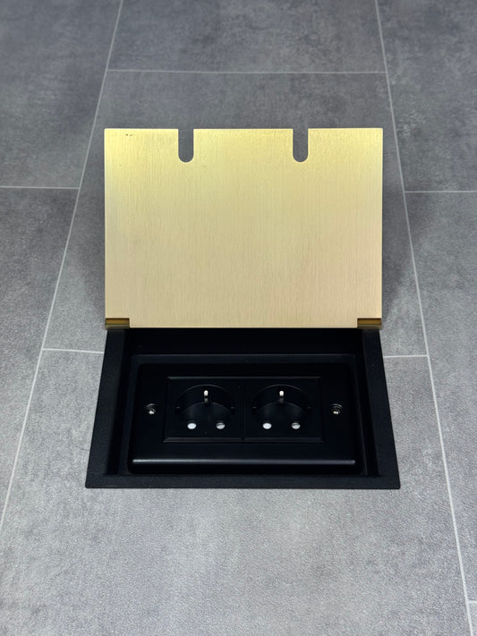 A satin brass double recessed floor socket with two Schuko (European) sockets in a black base installed in a floor.
