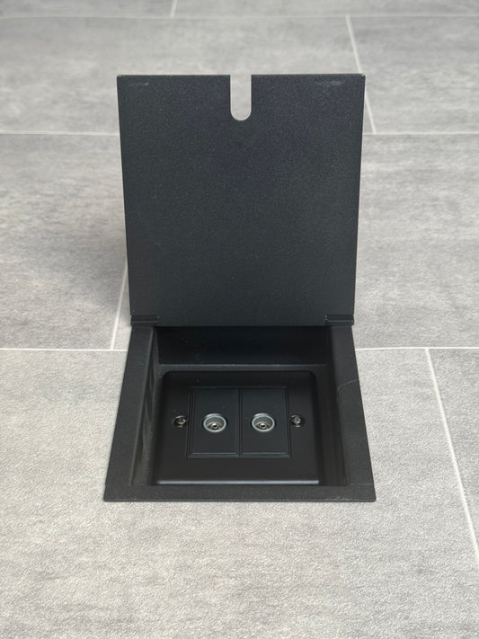 A matt black recessed floor socket with a double (2 gang) TV socket, installed on a tiled floor.
