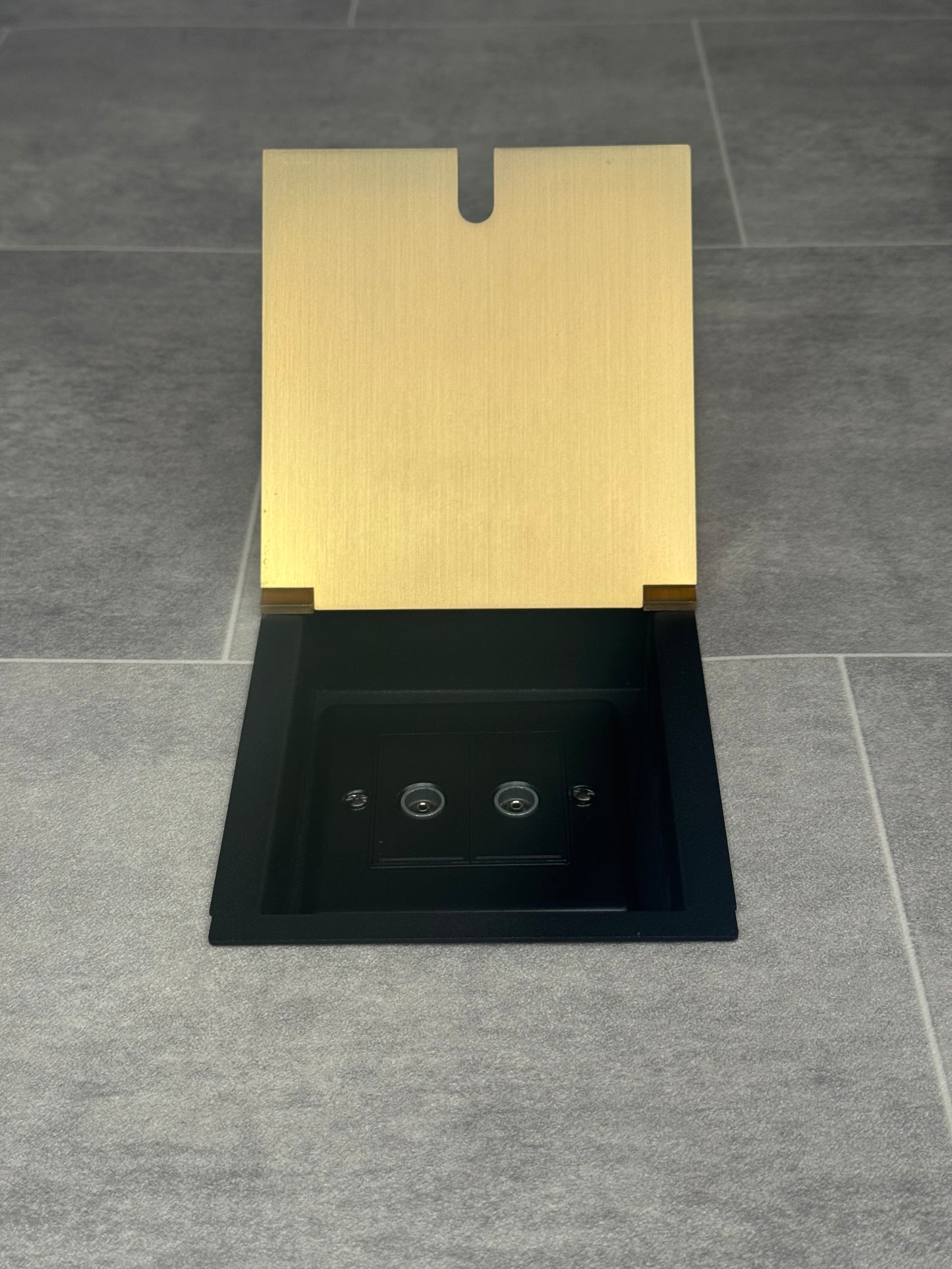 A satin brass recessed floor socket with a 2 gang TV socket, shown in an open position with the surrounding floor visible.