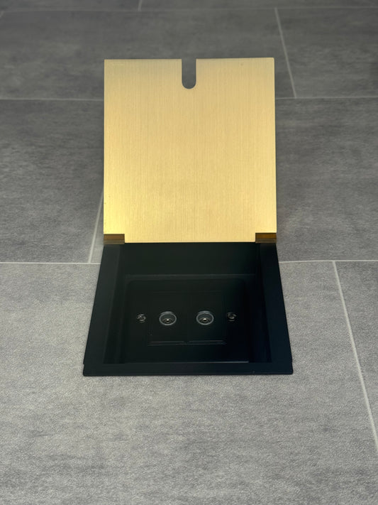 A satin brass recessed floor socket with a 2 gang TV socket, shown in an open position with the surrounding floor visible.