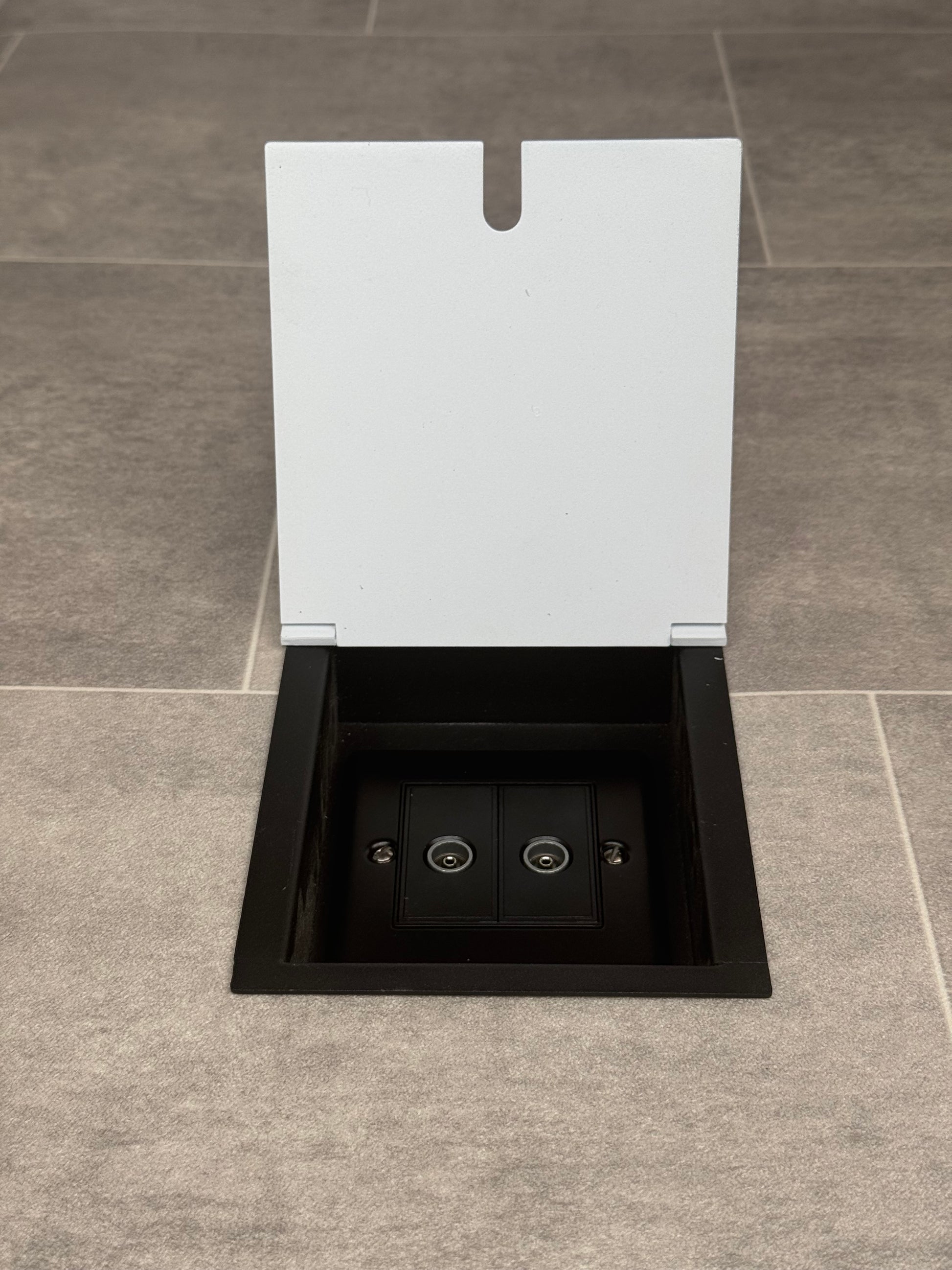 A white recessed floor socket with a opened lid revealing a 2 gang (double) TV socket inside.