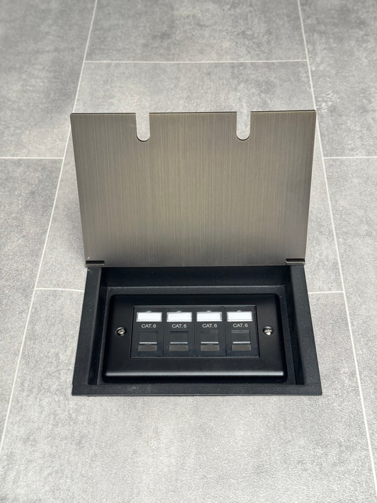 A recessed floor socket in antique brass with a double box design, including 4 gang RJ45 cat6 sockets, opened and set in a tiled floor.
