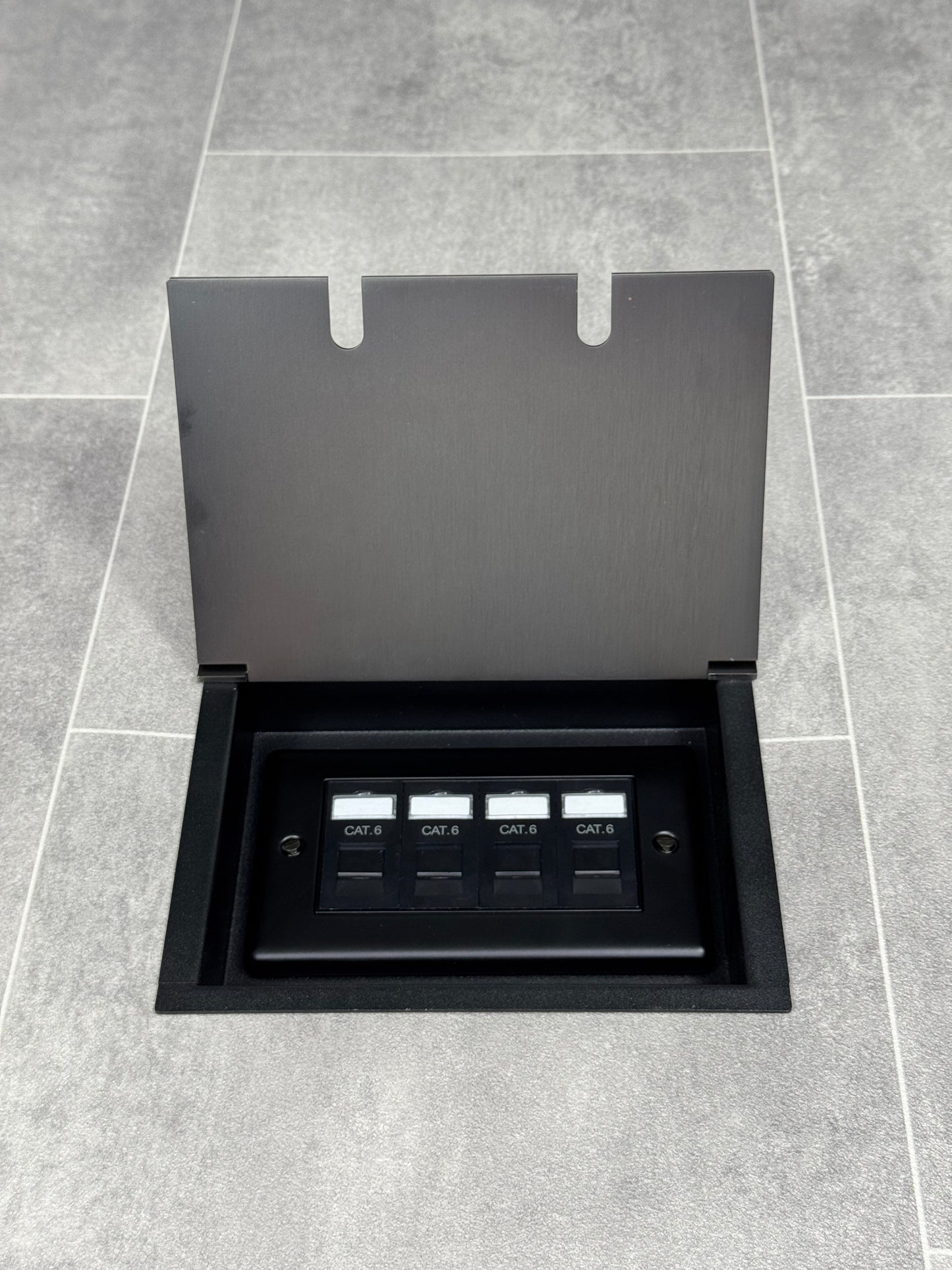 Old bronze double recessed floor socket with a black base installed on a grey floor, opened to show the 4 gang RJ45 cat6 socket.